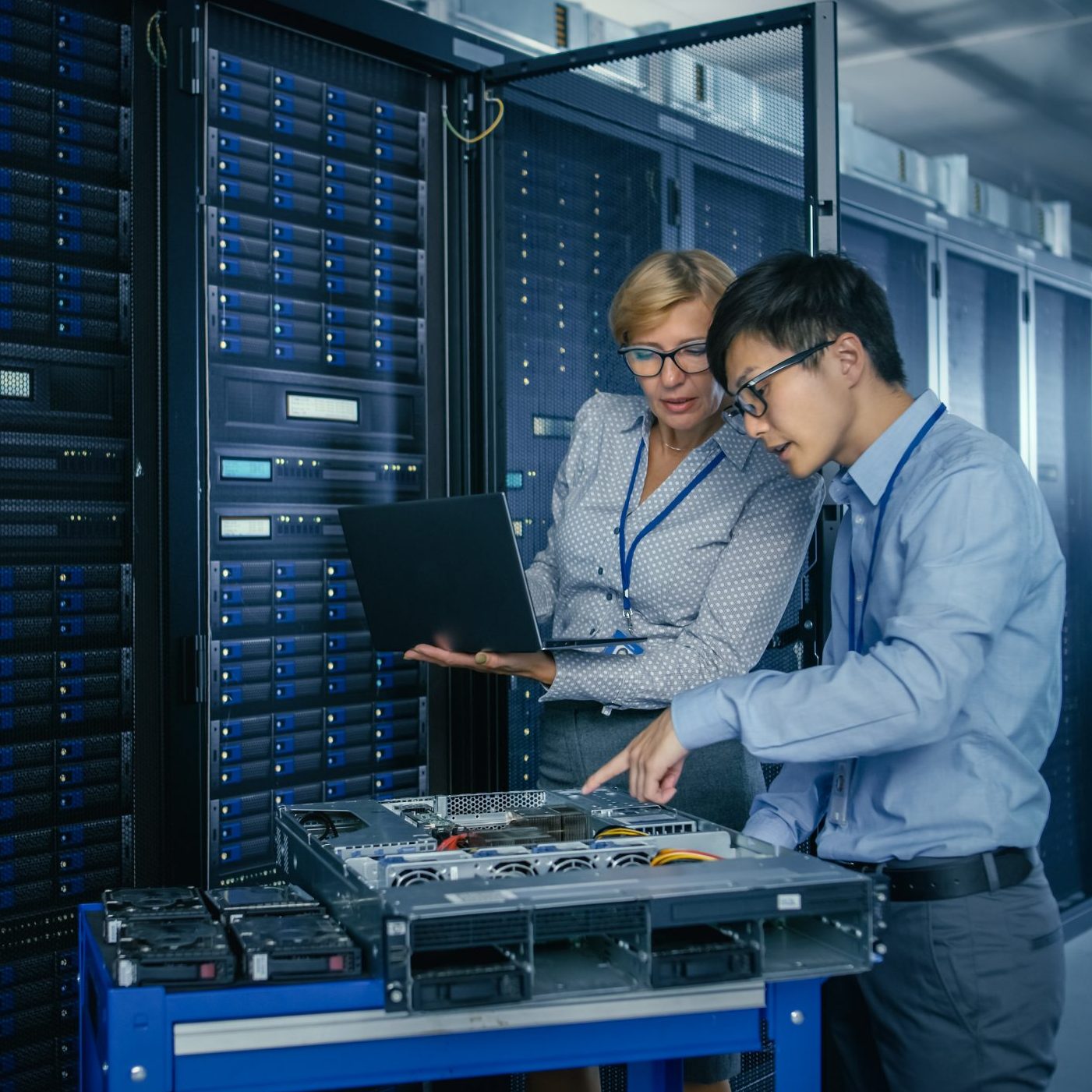 In the Modern Data Center: Engineer and IT Specialist Work with Server Racks, on a Pushcart Equipment for Installing New Hardware. Specialists Doing Maintenance and Diagnostics of the Database.